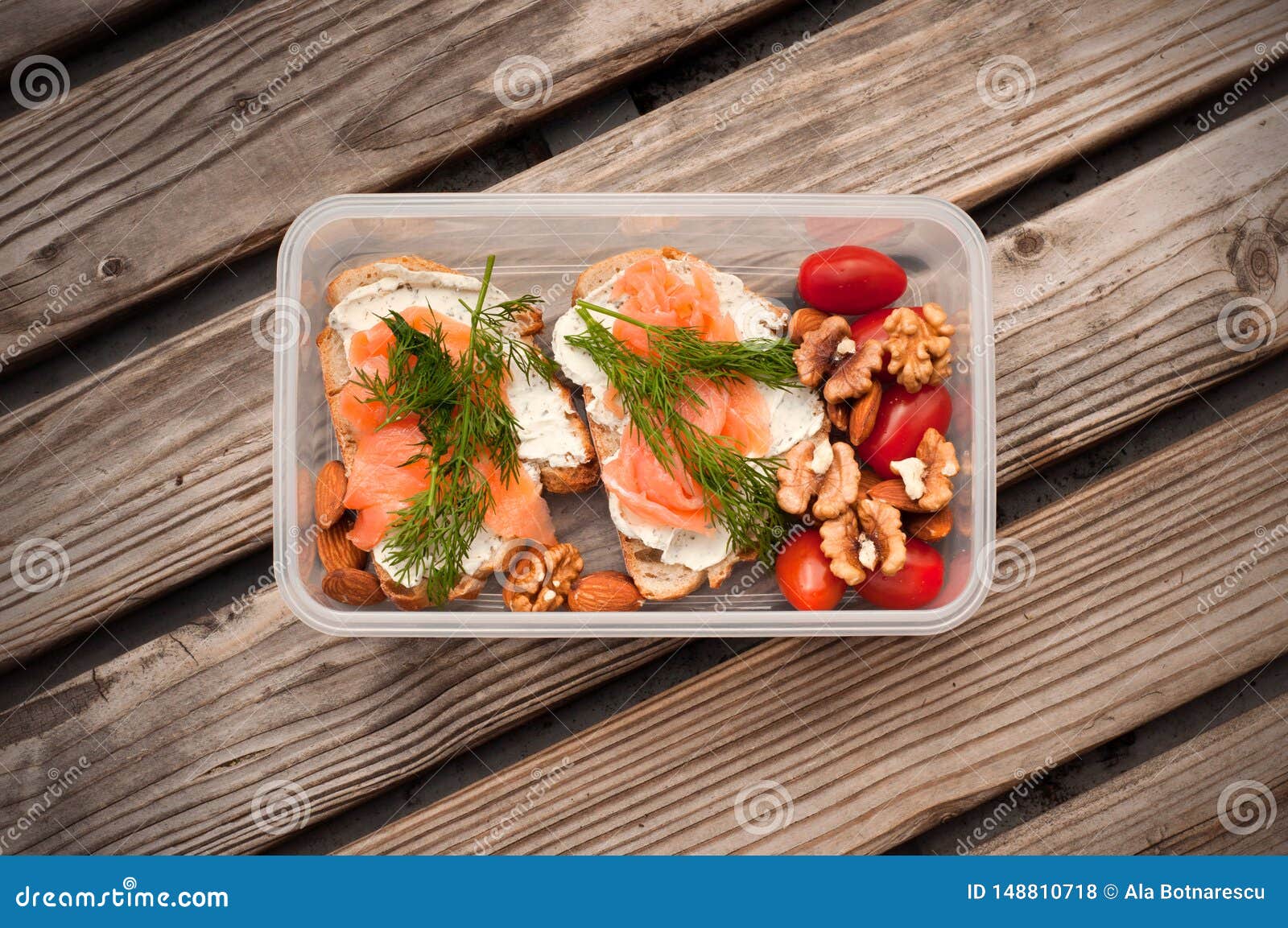 Wholemeal bread with cheese and salmon in a plastic container. Dill and almond with cherry tomatoes. Healthy sandwiches. Omega-3 for snack. Proper nutrition. Sport food