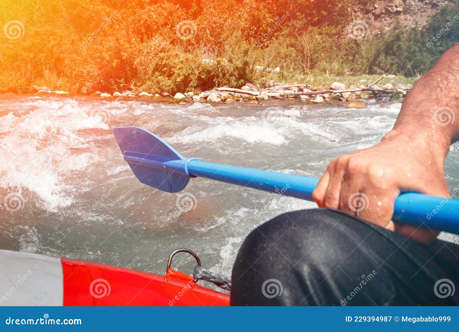 Paddle in Hand on the Edge of a Raft Rafting Down a Mountain River