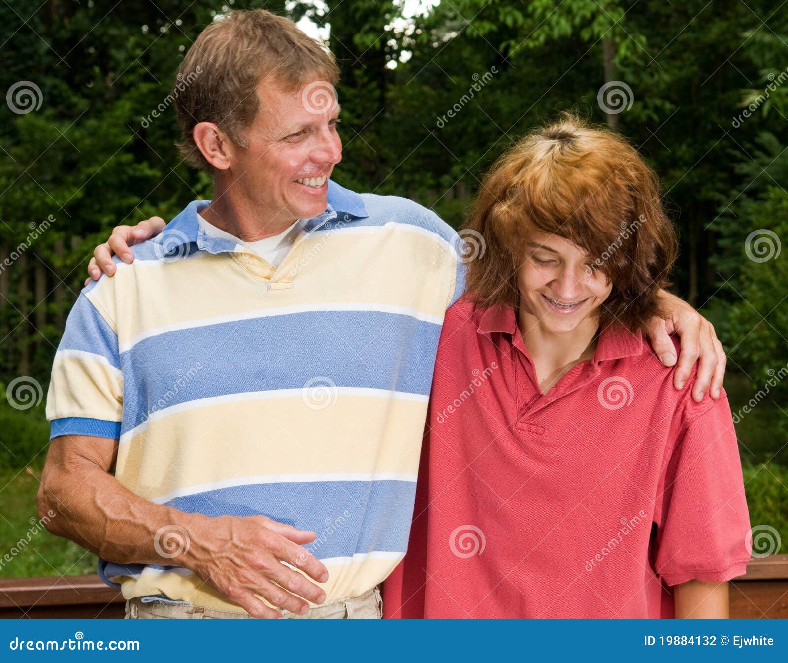 Pai e filho adolescente que são próximos. Pai e filho adolescente (com cabelo vermelho longo) que abraçam e que riem
