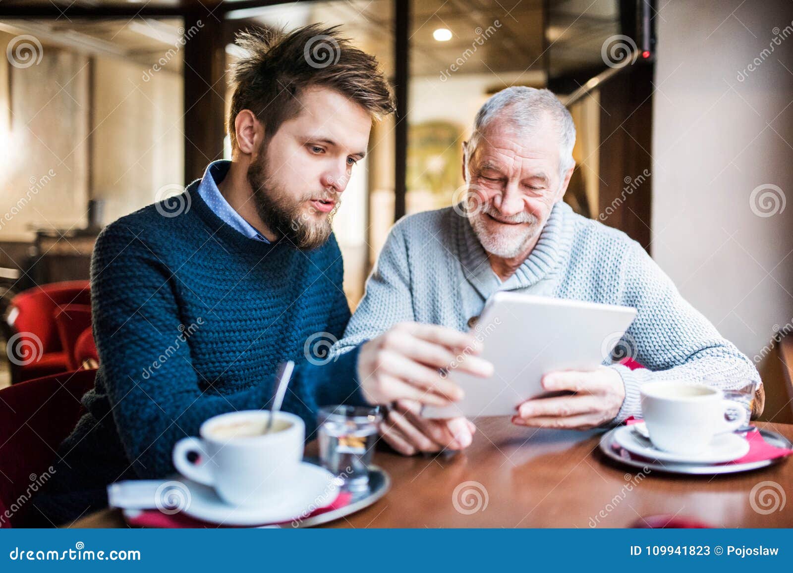 Pai superior e seu filho novo com tabuleta em um café