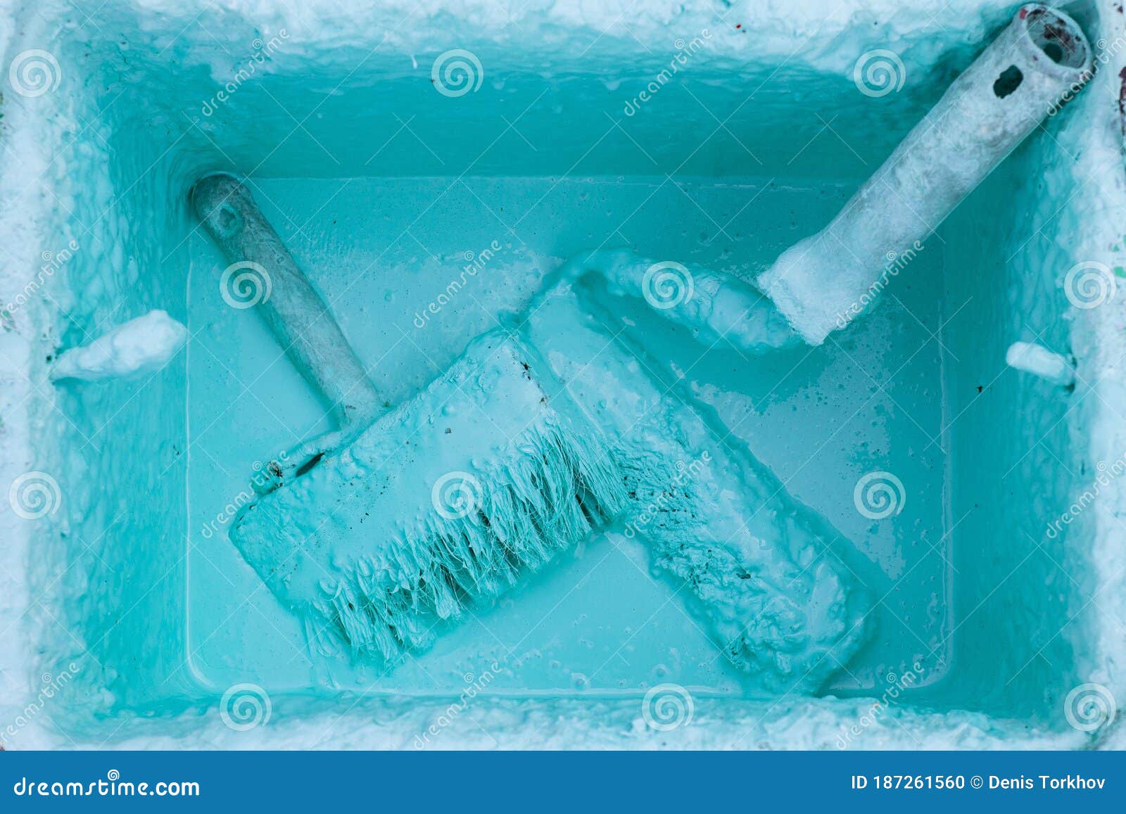Paint Roller and Brush in a Bucket with an Emulsion on Concrete Paving
