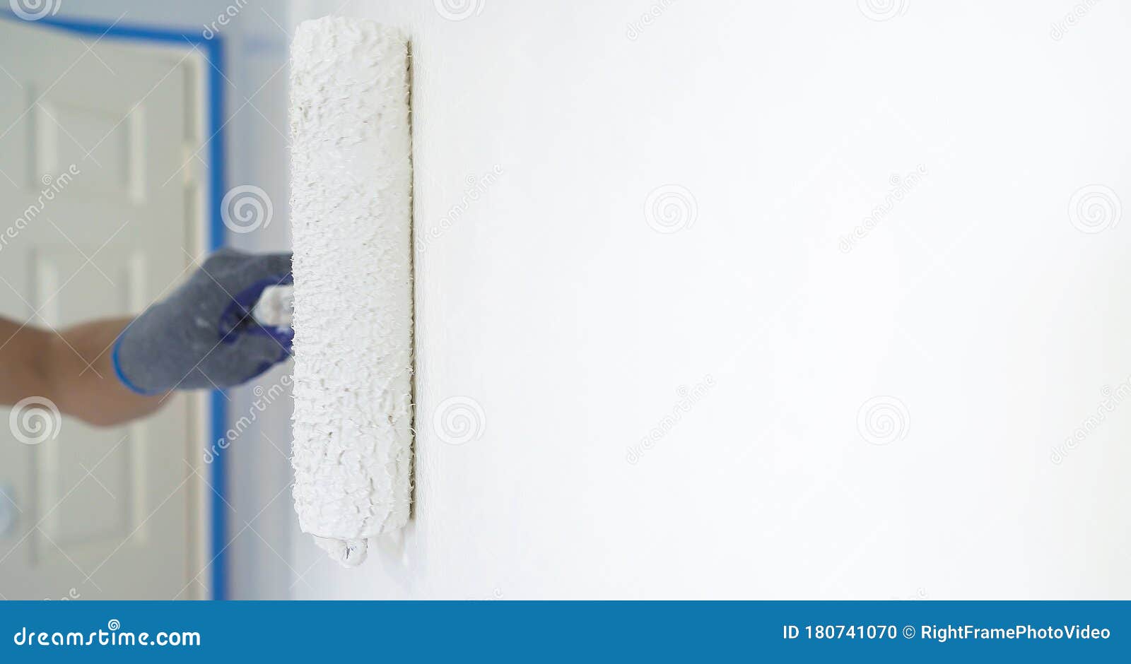 Painter Painting a House Wall with a White Paint Roller Stock Photo