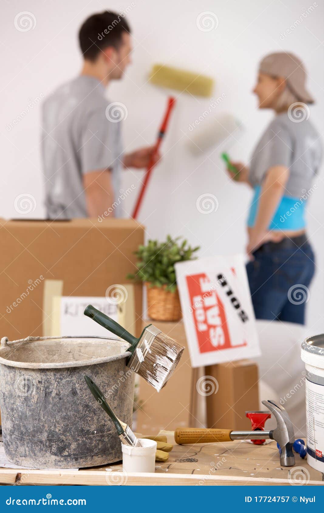 Painting new house. Young couple painting their new house with paint roller, equipment in focus.