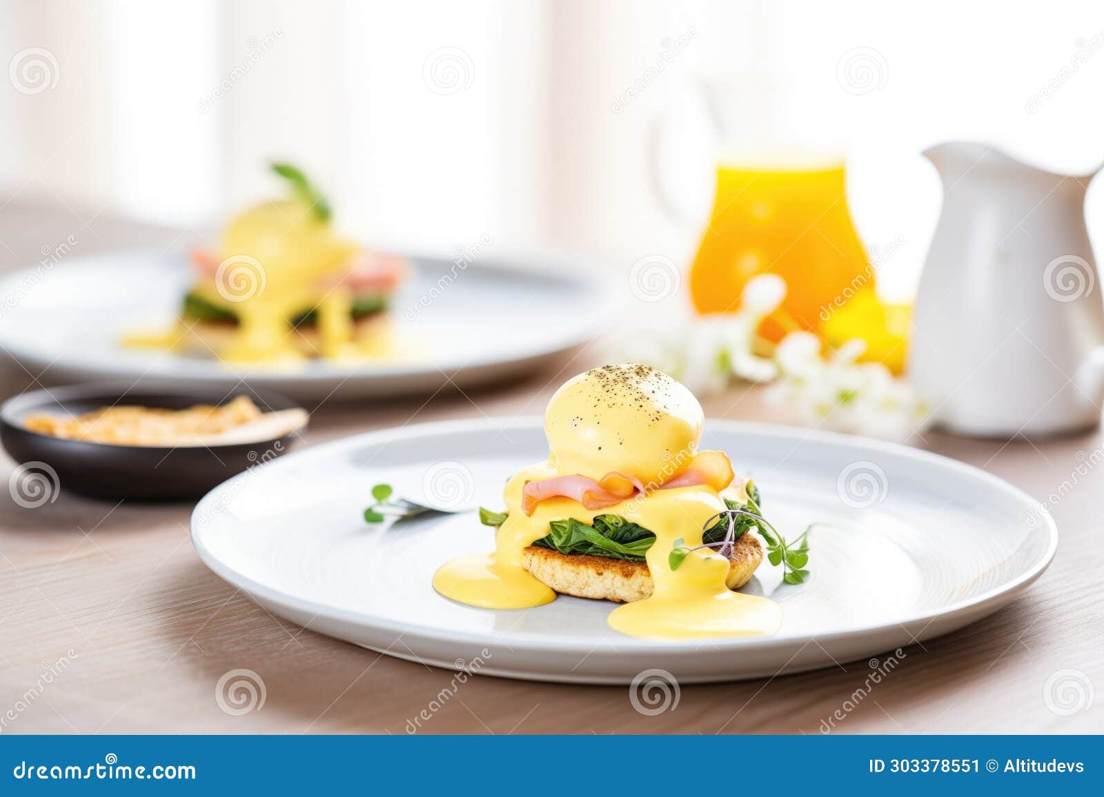 a pair of eggs benedicts on a plate with a small bowl of hollandaise