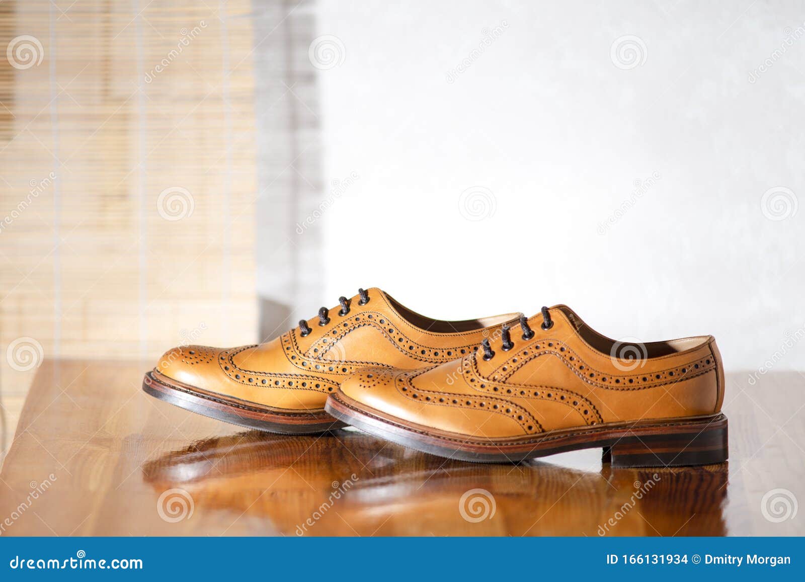 pair of male full brogued tan oxford shoes. placed together on laqured table indoors