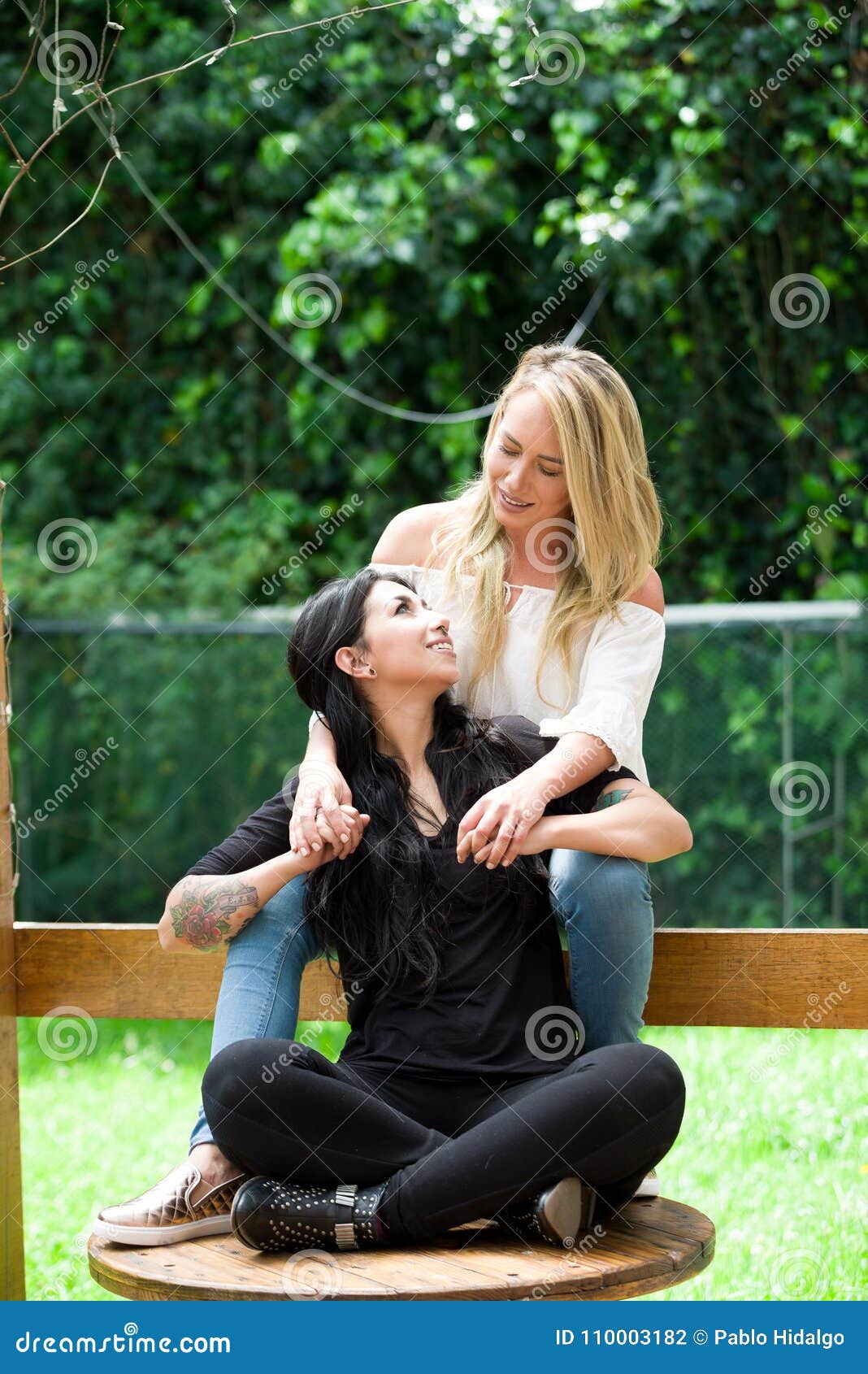 A Pair Of Proud Lesbian In Outdoors Sitting On A Wooden Table Blonde Woman Is Hugging A