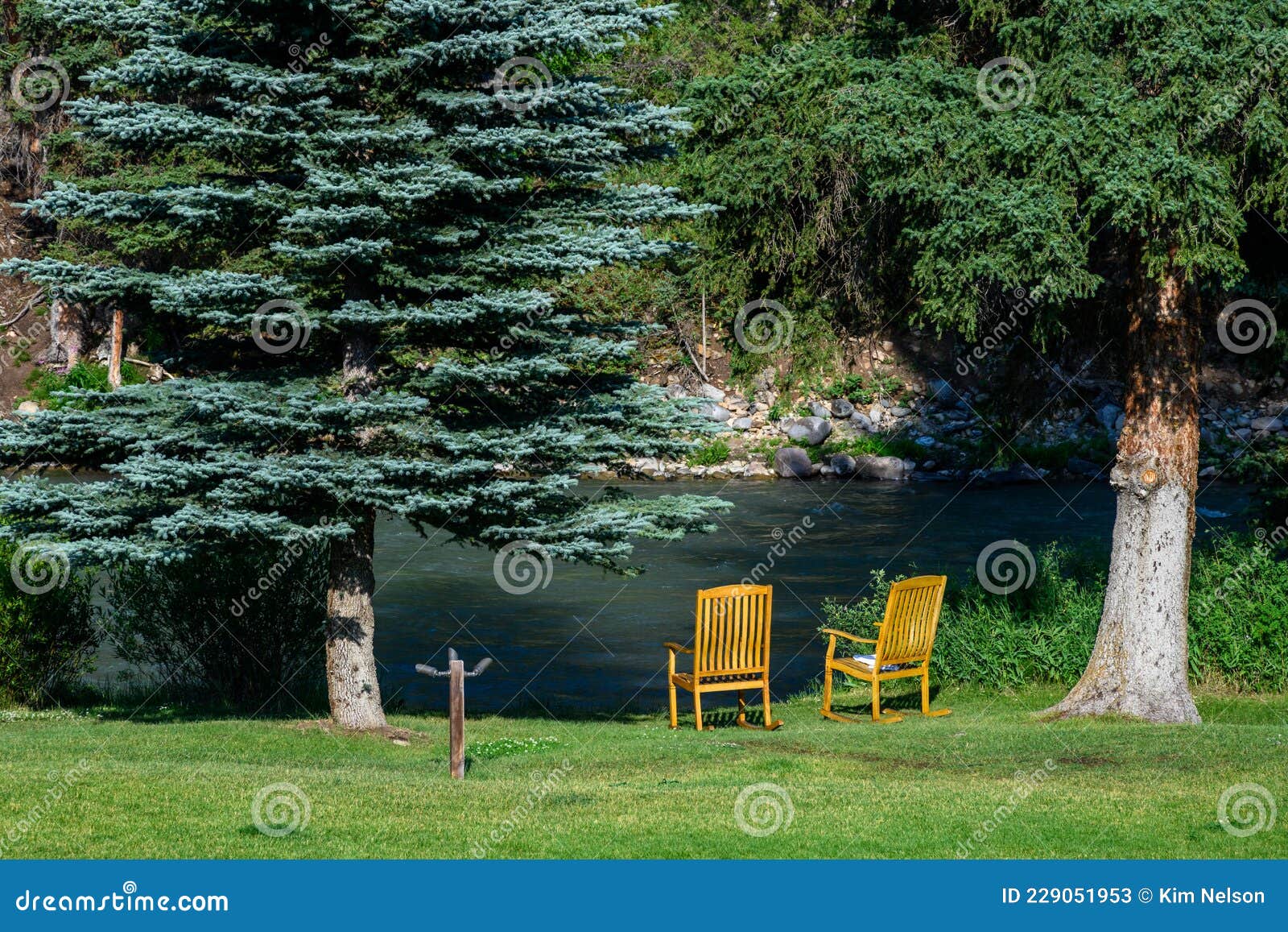 pair of wooden rocking chairs on a green lawn at the edge of the gallatin river
