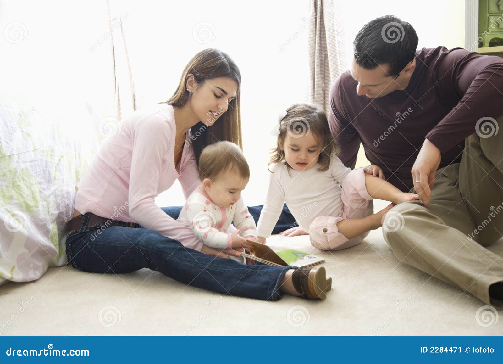 Pais e crianças. As crianças fêmeas caucasianos com a matriz e o pai que sentam-se no quarto pavimentam a vista do livro.