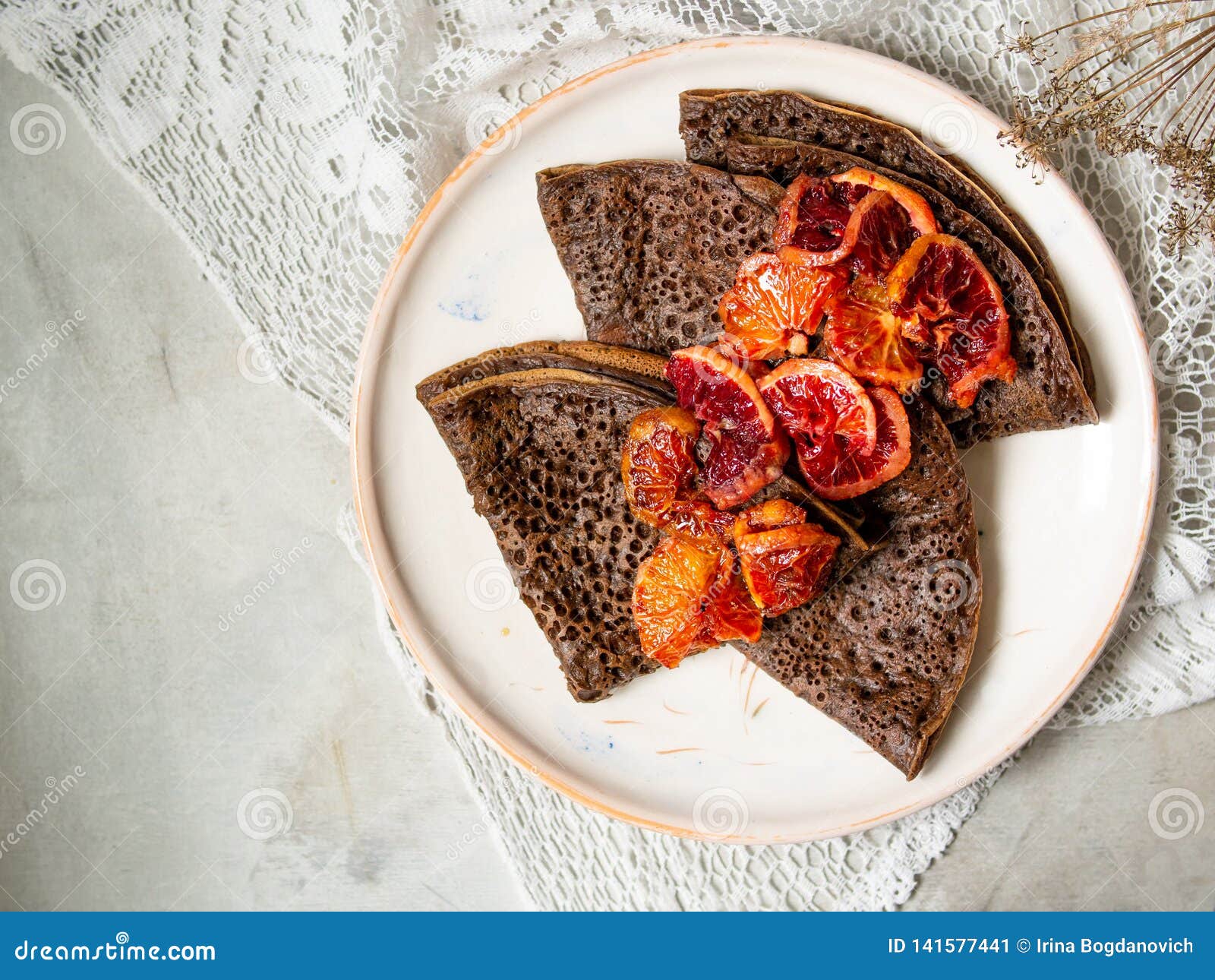 Pancake sottili del cioccolato con la salsa delle arance sanguinelle su un piatto bianco su fondo grigio con il tessuto del pizzo Pila di crêpe, blin russo, Maslenitsa Fine saporita della prima colazione su, fuoco selettivo