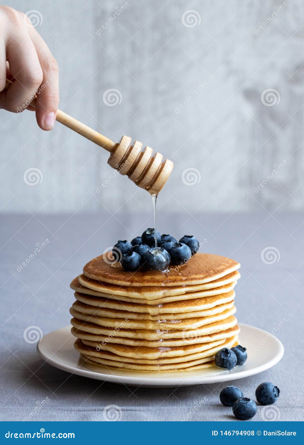 Pancakes with blueberries and honey of acacia on a neutral background. Pancakes with blueberries and honey of acacia on a light plate on a neutral background. In the hand of the child is a wooden spoon with flowing honey.