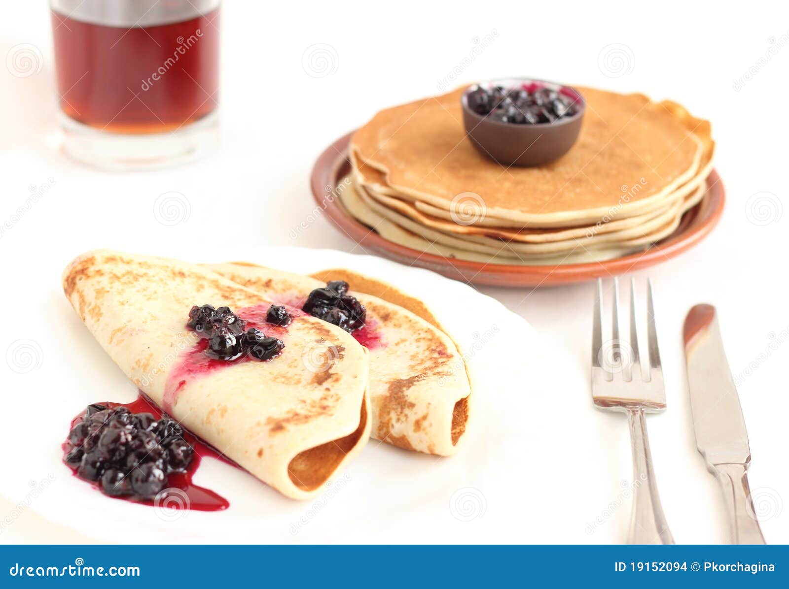 Pancakes on a plate with black currant jam on white background