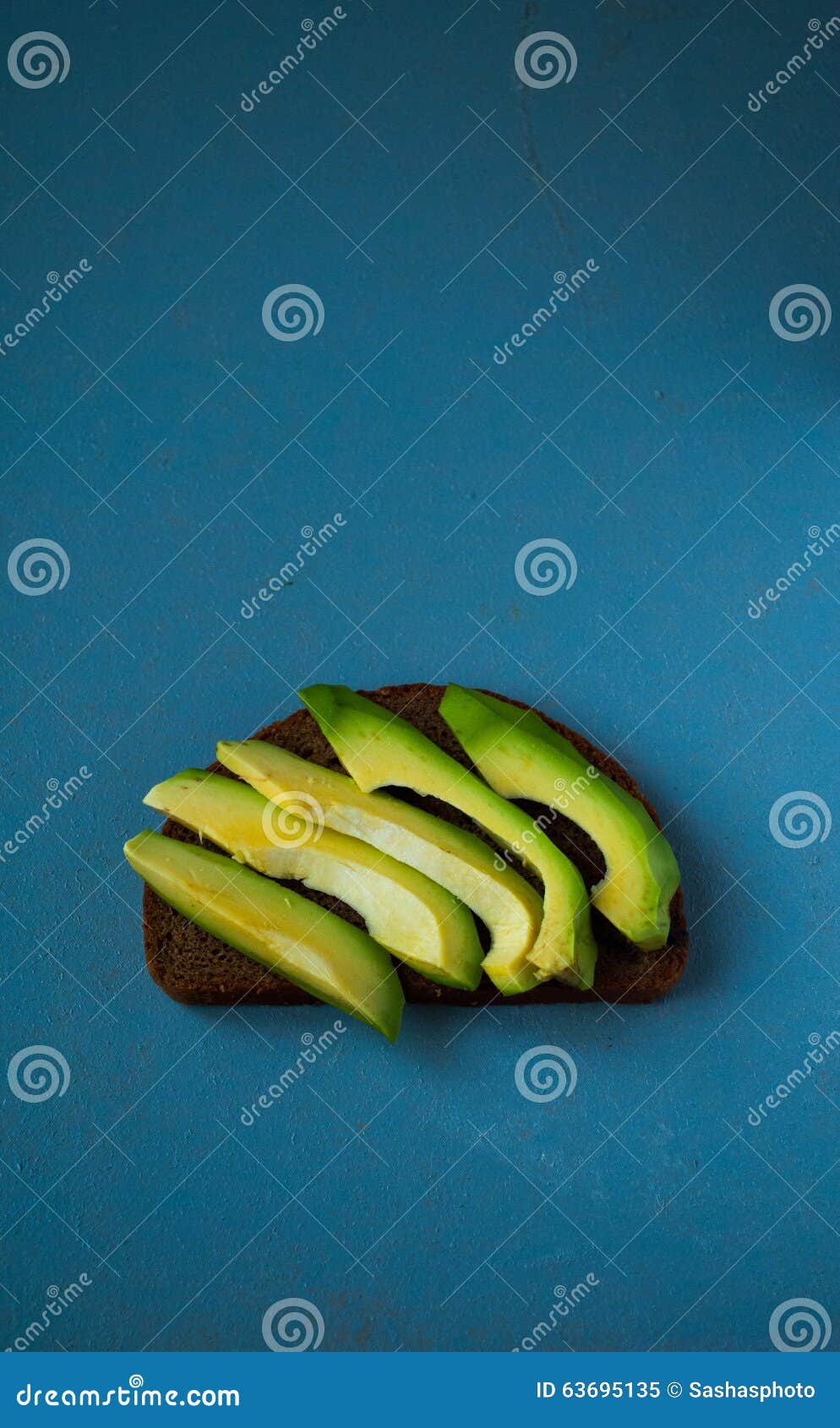 Panino dell'avocado sul pane di segale scuro. Panino con le fette di avocado sul pane di segale nel centro della tavola
