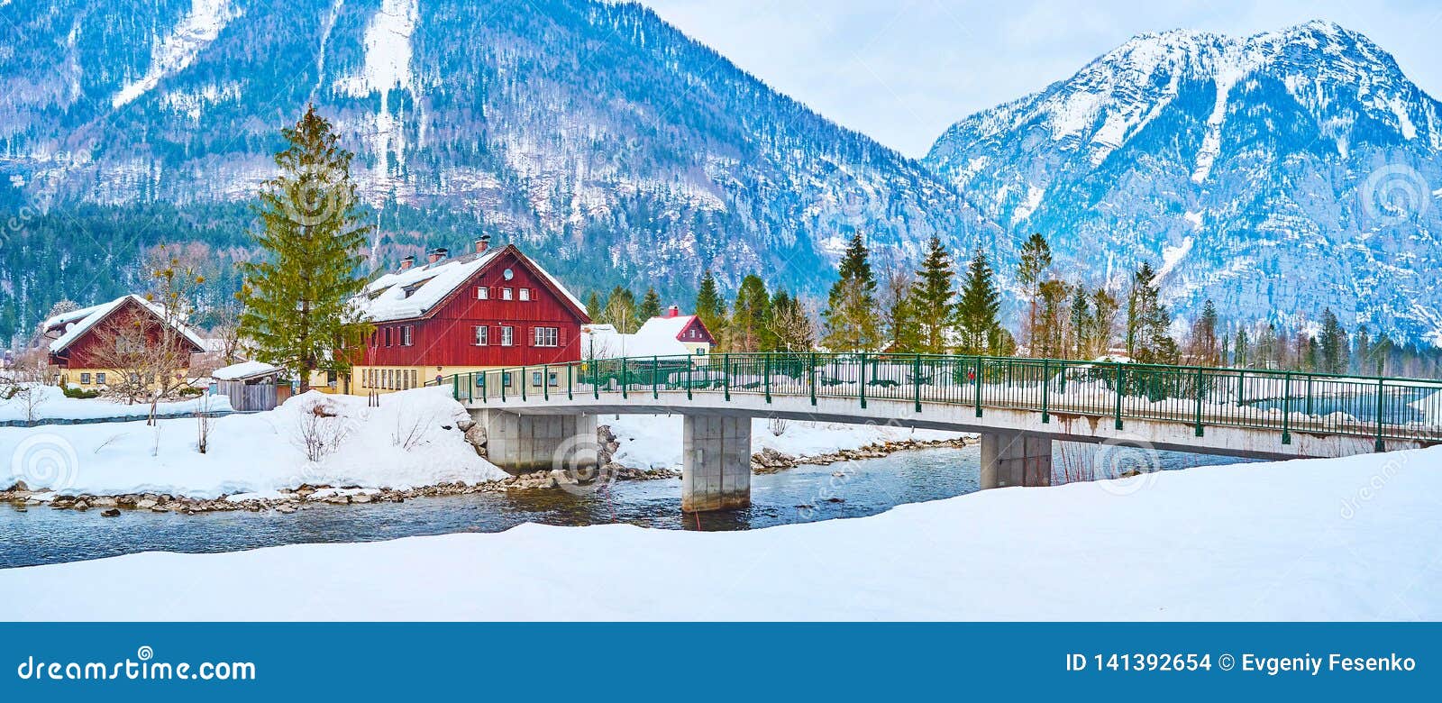 Panorama av det Obertraun vinterlandskapet, Salzkammergut, Österrike. Panorama av den Obertraun byn från den snöig banken av den Traun floden med gräsplan sörjer och enorma fjällängberg på bakgrund, Salzkammergut, Österrike