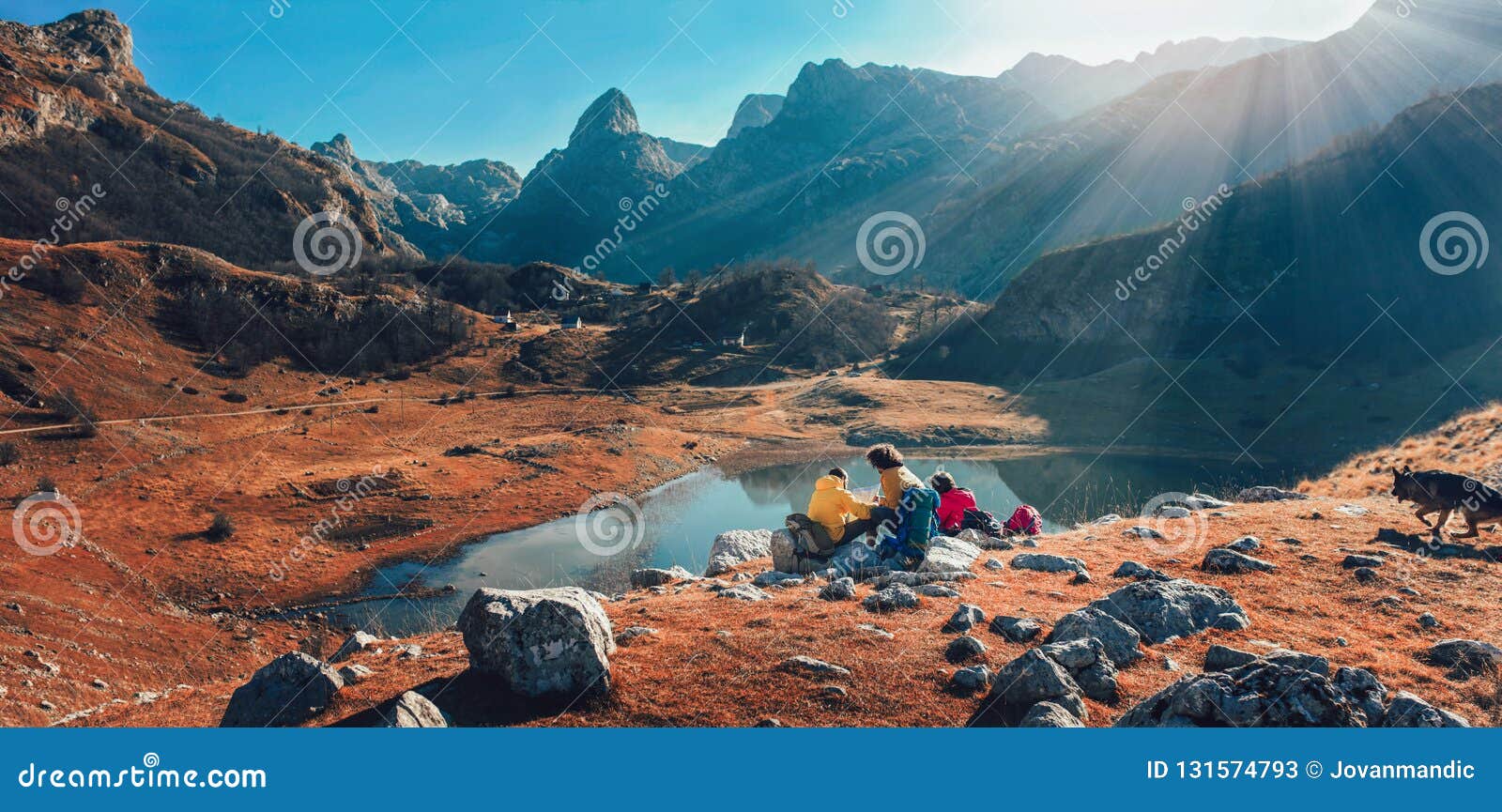 Panorama view on group of hikers enjoying view on mountain lake. Young people hiking in nature