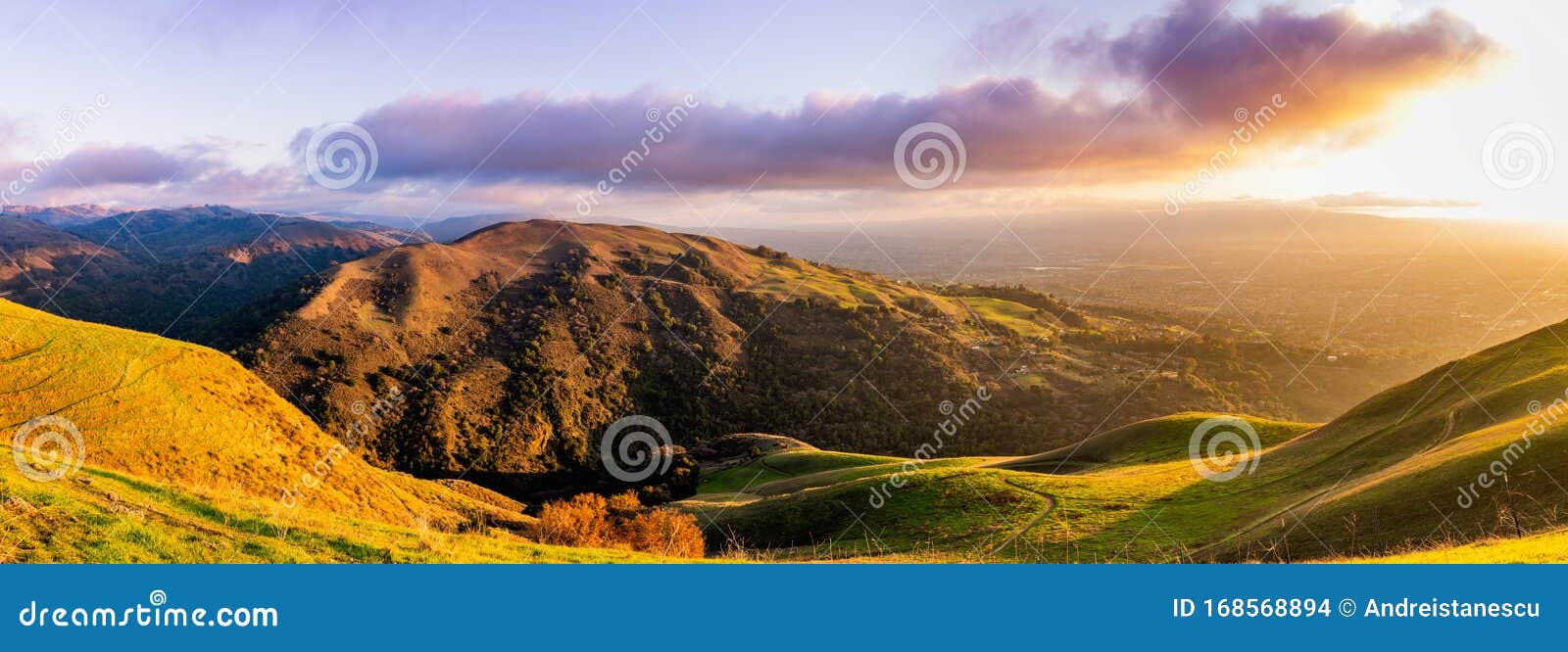 panoramic sunset view of hills and valleys in the diablo mountain range starting to turn green; san jose and bright light from the