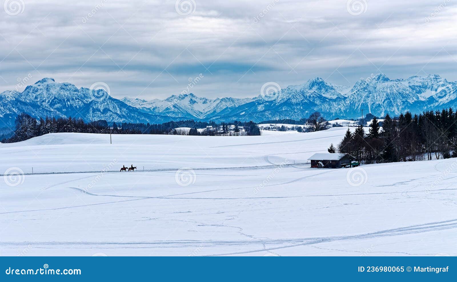 panoramic view over snowy pre-alpine landscape with two riders on horses