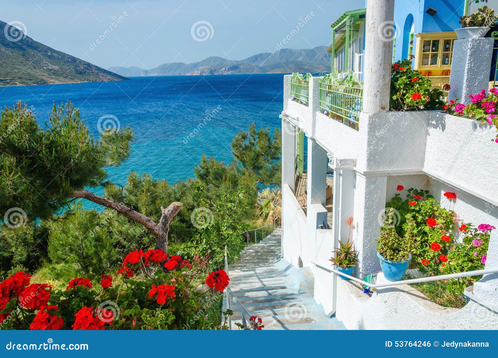 Panoramic view on typical Greek studio with flowers and white teracce having clear view on sea landspace with islands, Greece