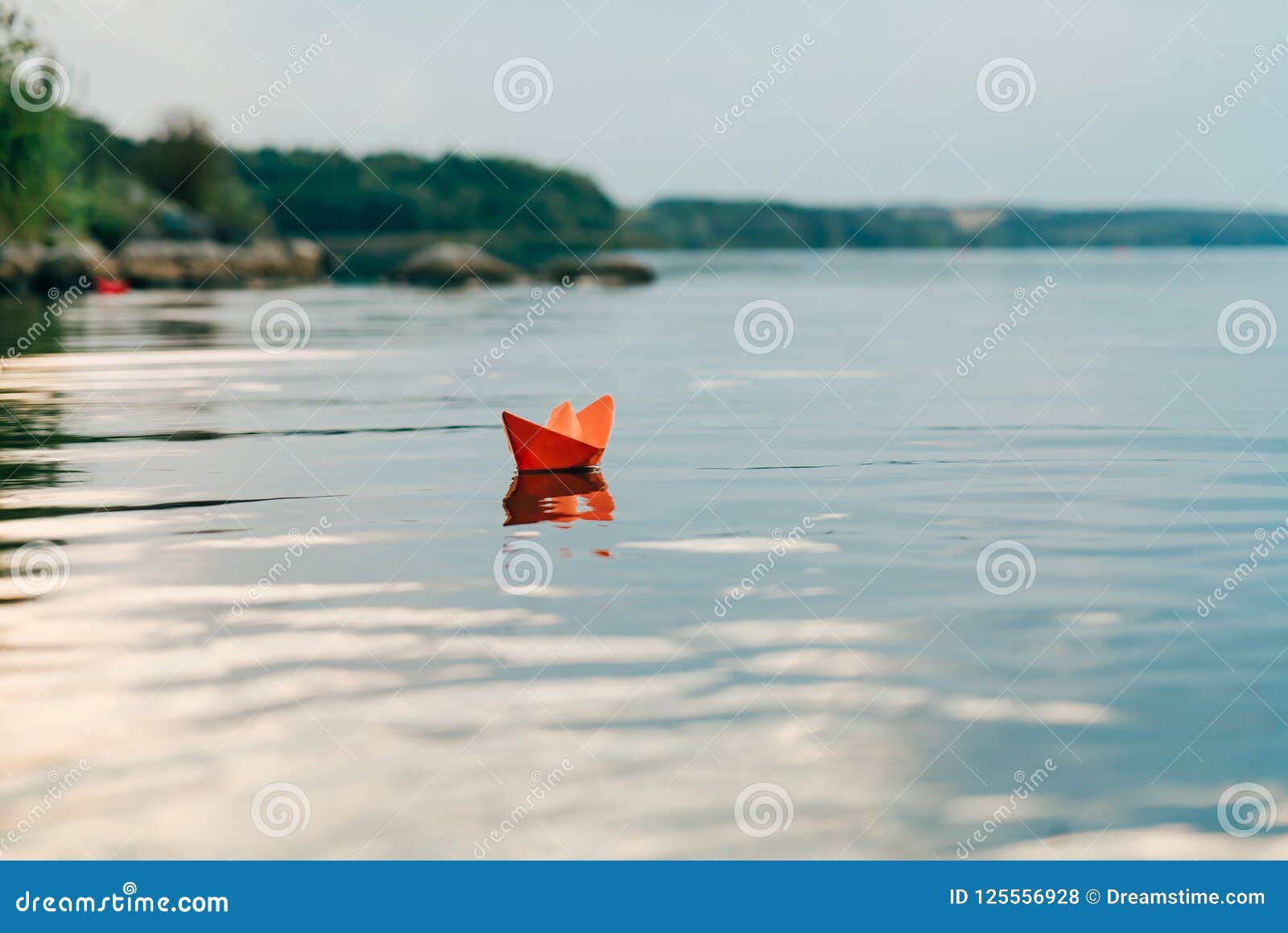 a paper boat sails by the river in the summer. it has an orange color and floats downstream along the shore