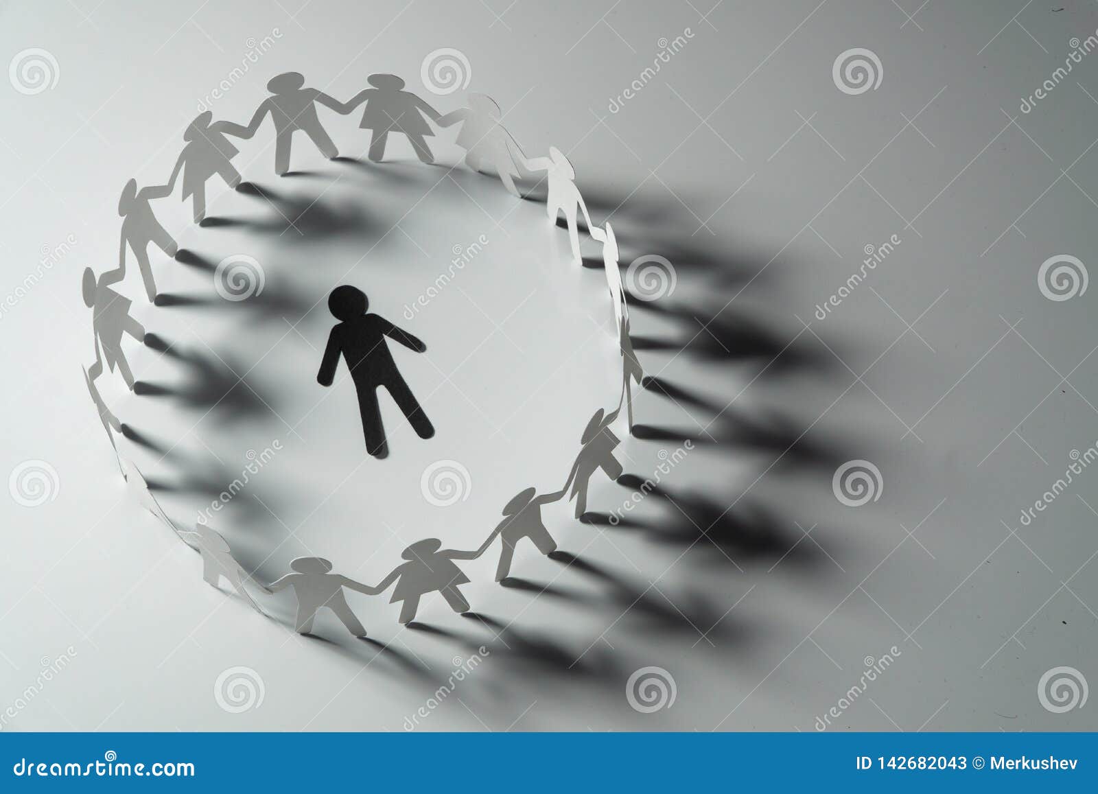 paper human figure surrounded by circle of paper people holding hands on white surface. bulling, segregation, conflict