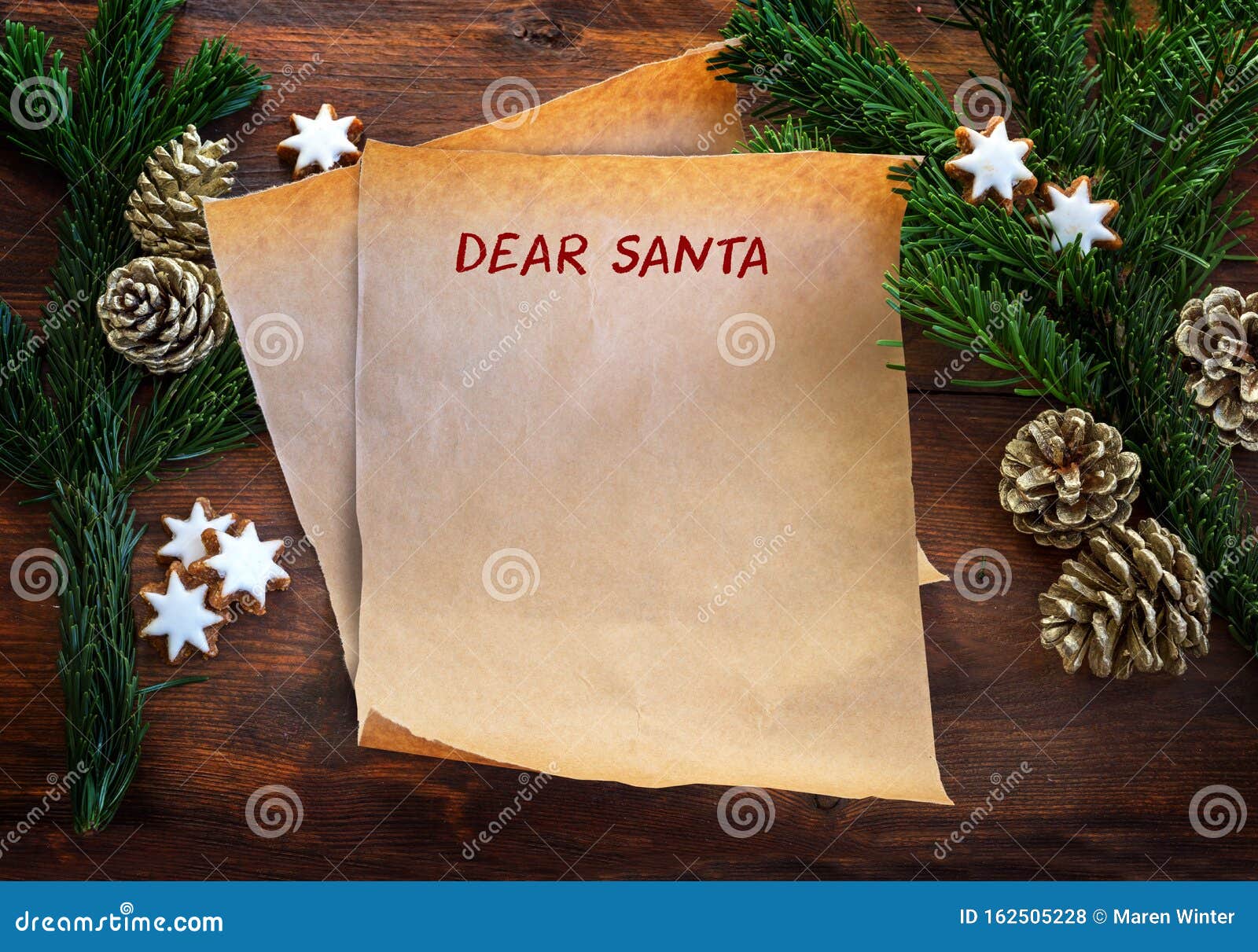 paper sheet with text dear santa, between fir branches, cinnamon stars and pine cones on rustic dark wood, christmas wish list or