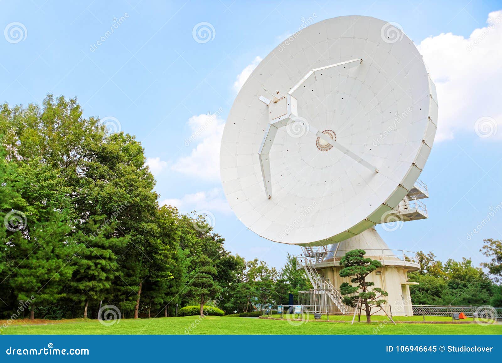 parabolic antenna at the top of a hill with trees near it and a clear sky on background