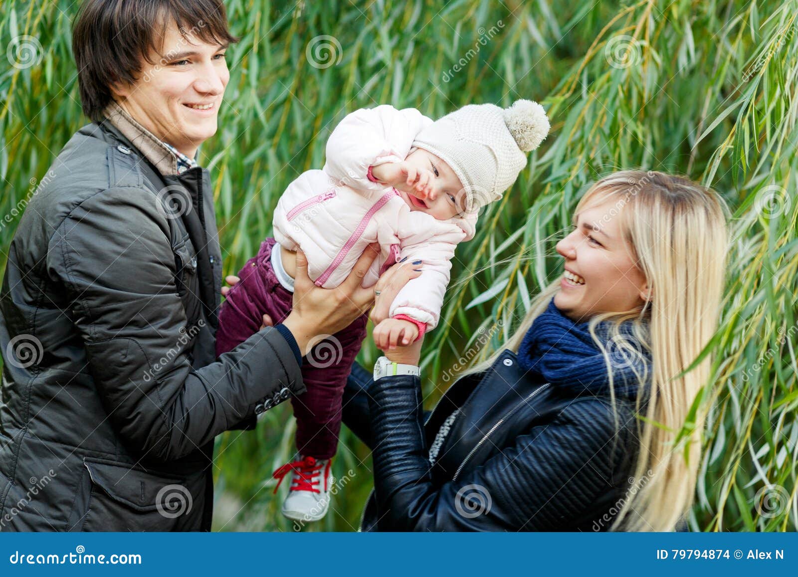 Parents Holding Baby Daughter in Park Near Trees Stock Photo ...