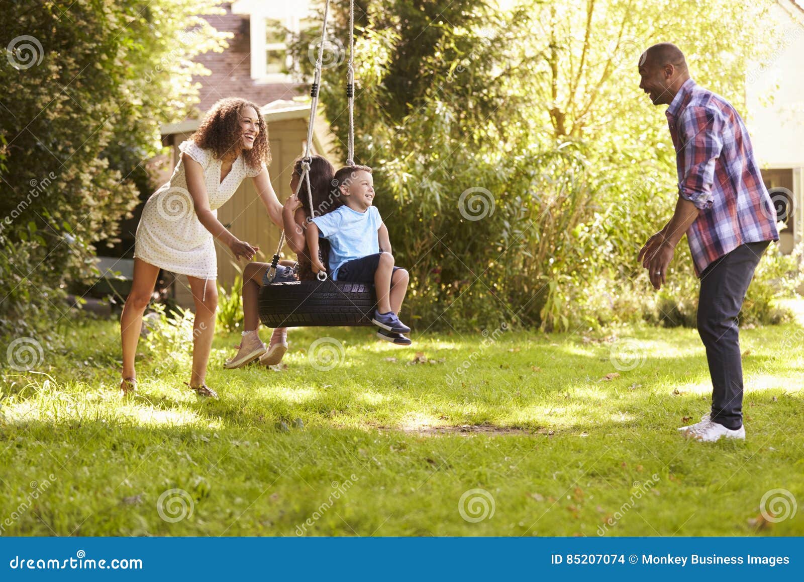 Parents Pushing Children on Tire Swing in Garden Stock Photo - Image of ...