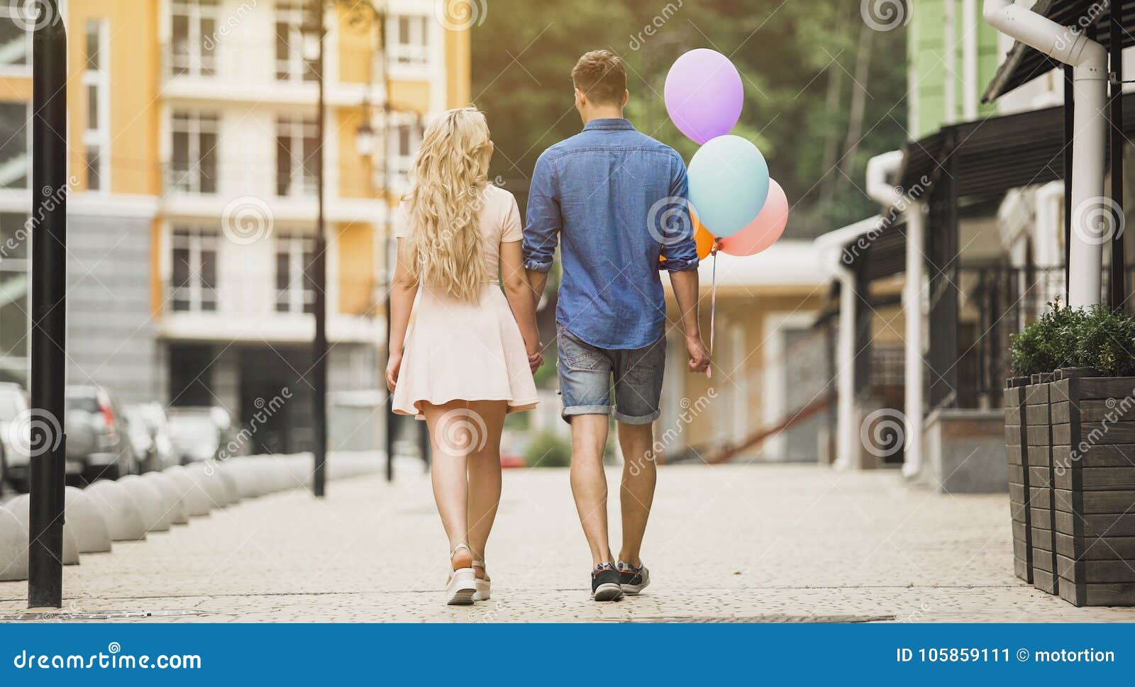 Pares felices que caminan abajo de la calle de la ciudad, sosteniendo los globos coloridos, fecha romántica, vídeo común