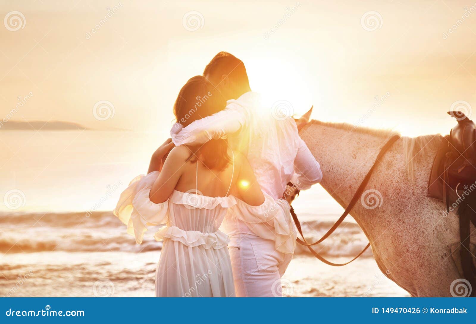Pares jovenes que caminan un caballo majestuoso, blanco - paisaje de la playa