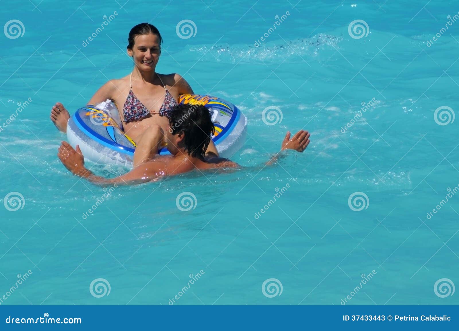 Pares no anel de flutuação. Pares felizes que têm o divertimento com anel de flutuação no mar azul