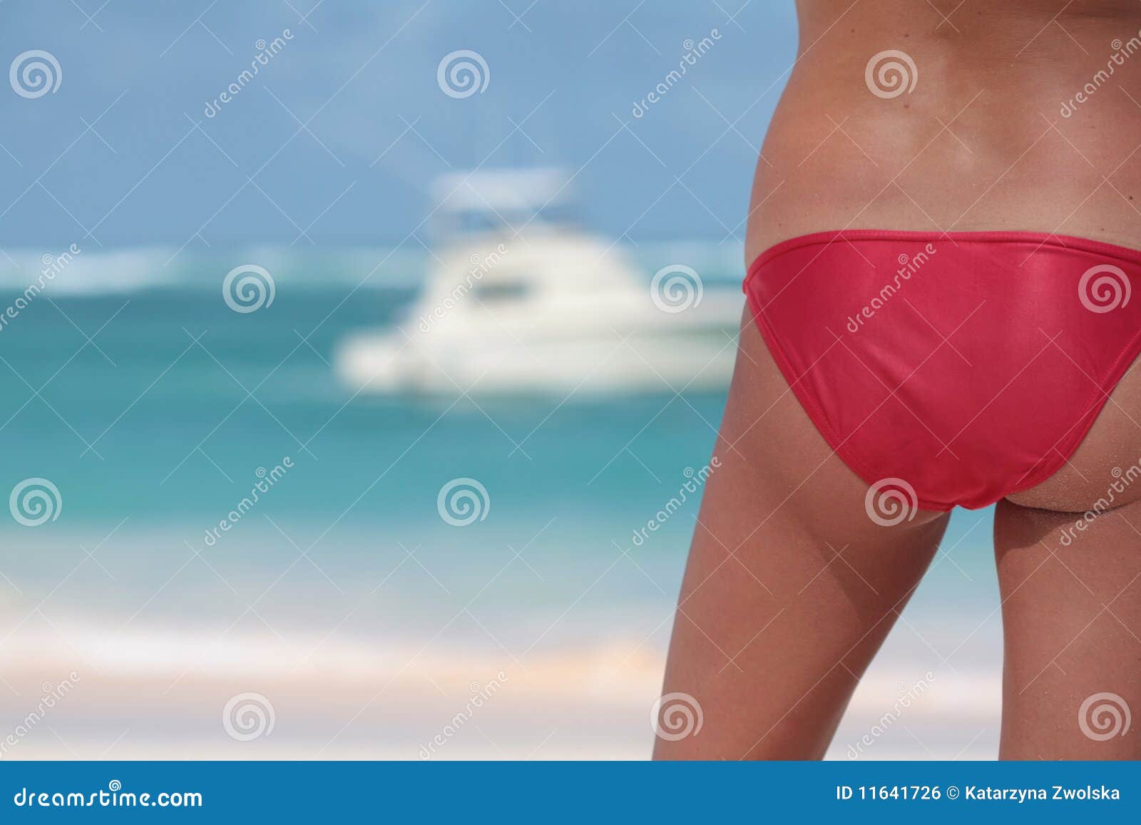 Parte traseira da mulher no biquini vermelho na praia tropical. Parte traseira da mulher no biquini vermelho na face da praia ao oceano com o barco no fundo