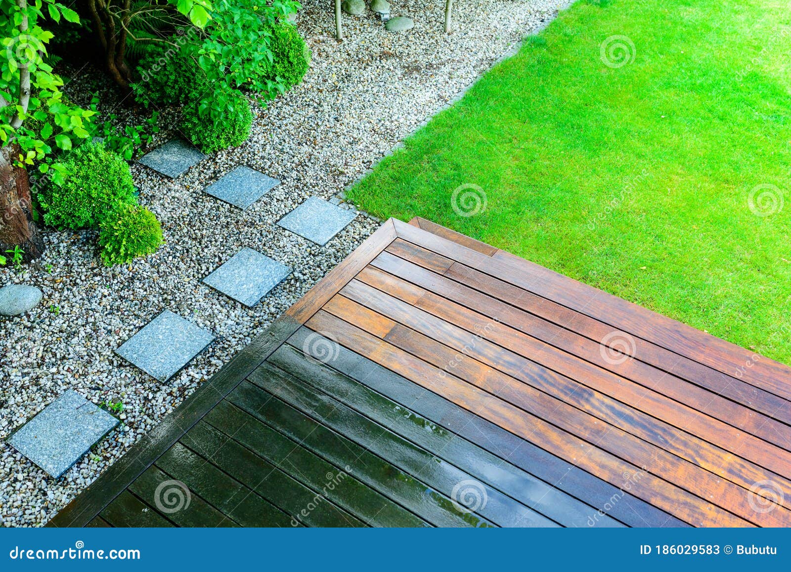 partially cleaned wooden terrace with a pressure washer by the green lawn