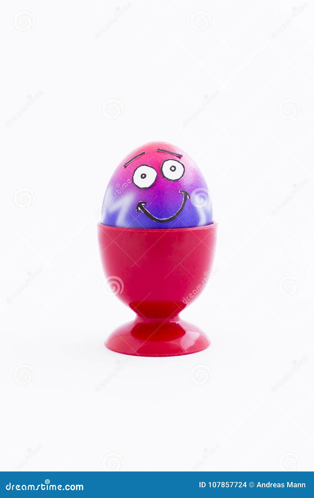 Partito di Pasqua con l'uovo pazzo. Il rosa e la porpora hanno dipinto l'uovo di Pasqua con il fronte divertente di stile del fumetto in un portauovo di plastica rosso ed in un fondo bianco
