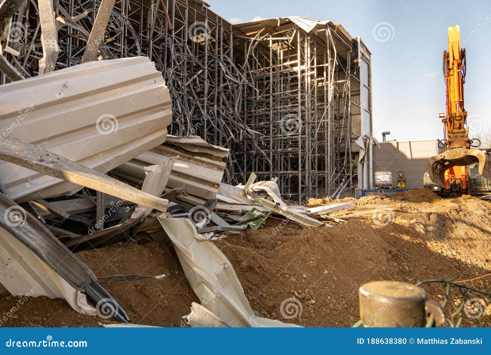 parts of the ruins of a partially demolished high-bay warehouse with a demolition excavator in the background