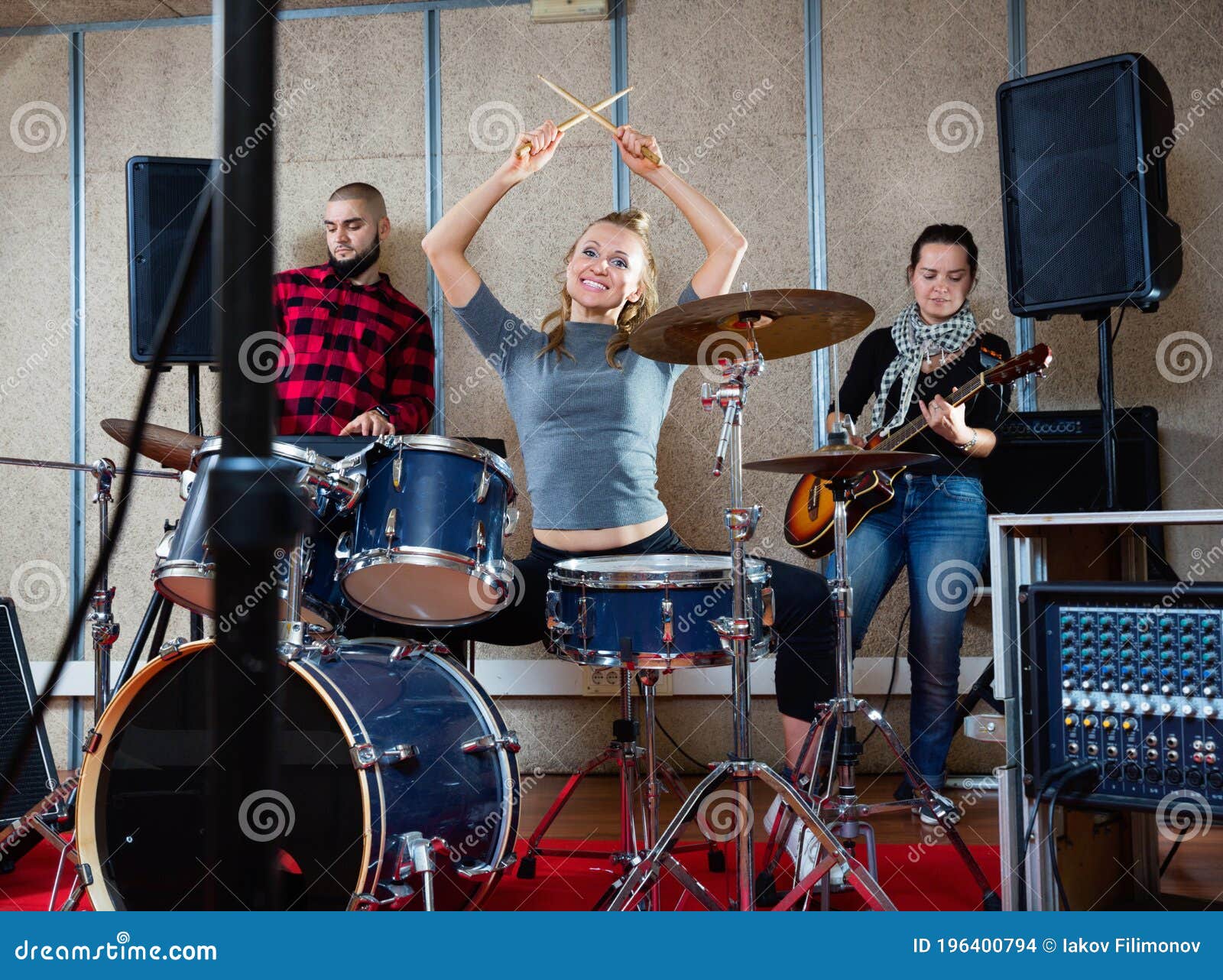 passionate emotional female drummer with her bandmates practicing in rehearsal room