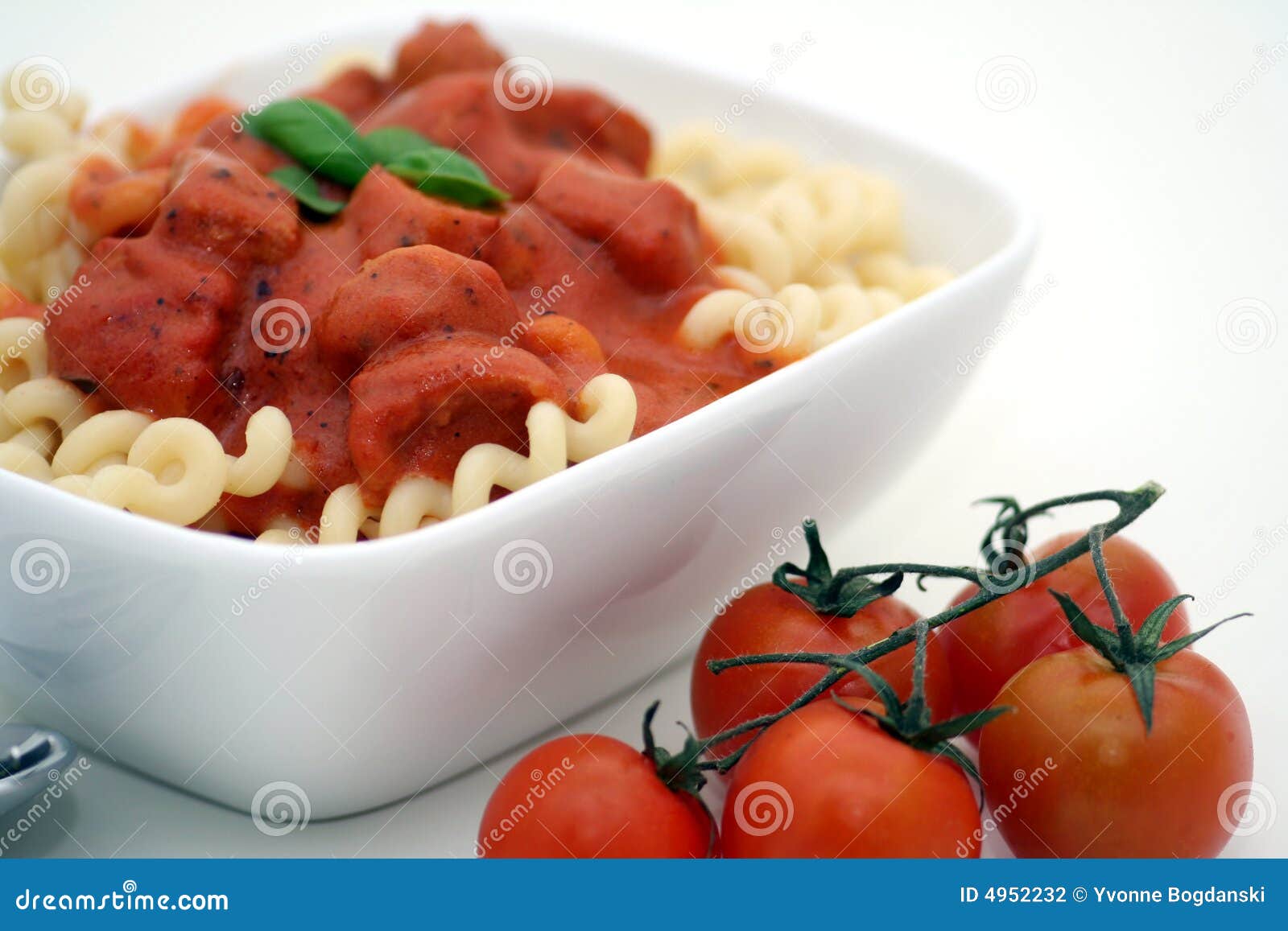 Delicious pasta served in a white bowl with red tomatoes.