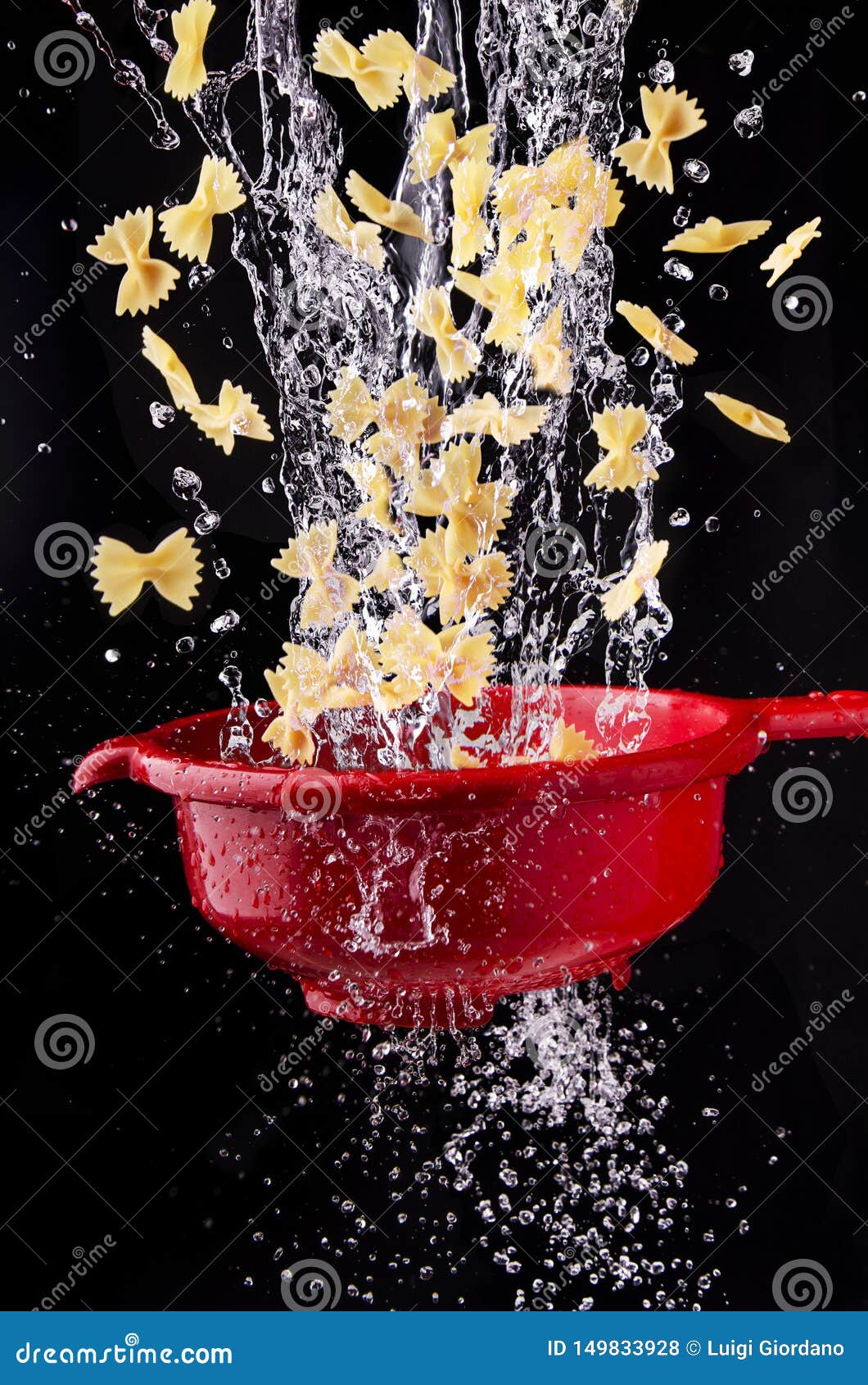 Pasta Falls into the Red Colander with Splashes of Water Stock Photo