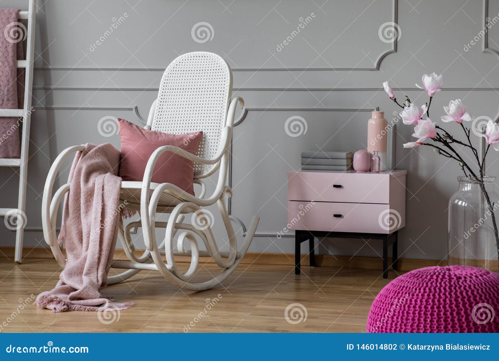 pastel pink blanket and pillow on white rocking chair in sophisticated room with nightstand and flowers in glass vase, copy space