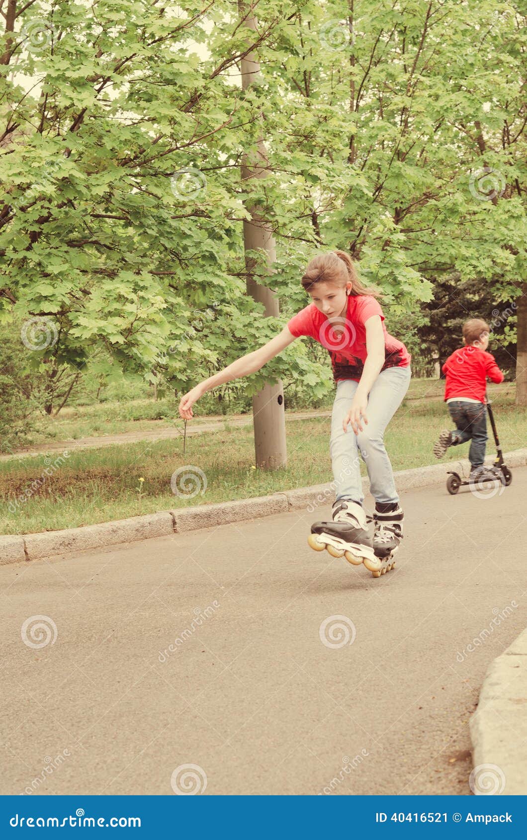Patinaje sobre ruedas experto atlético de la chica joven. El patinaje sobre ruedas joven experto atlético del adolescente en las cuchillas del rodillo en un muchacho joven del camino rural monta su vespa detrás de ella