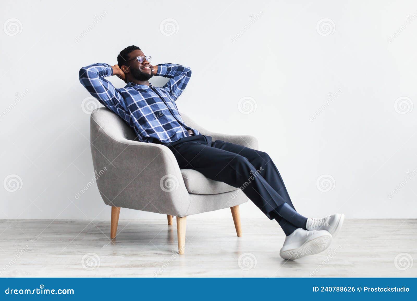 peaceful young black man relaxing in armchair against white studio wall, free space