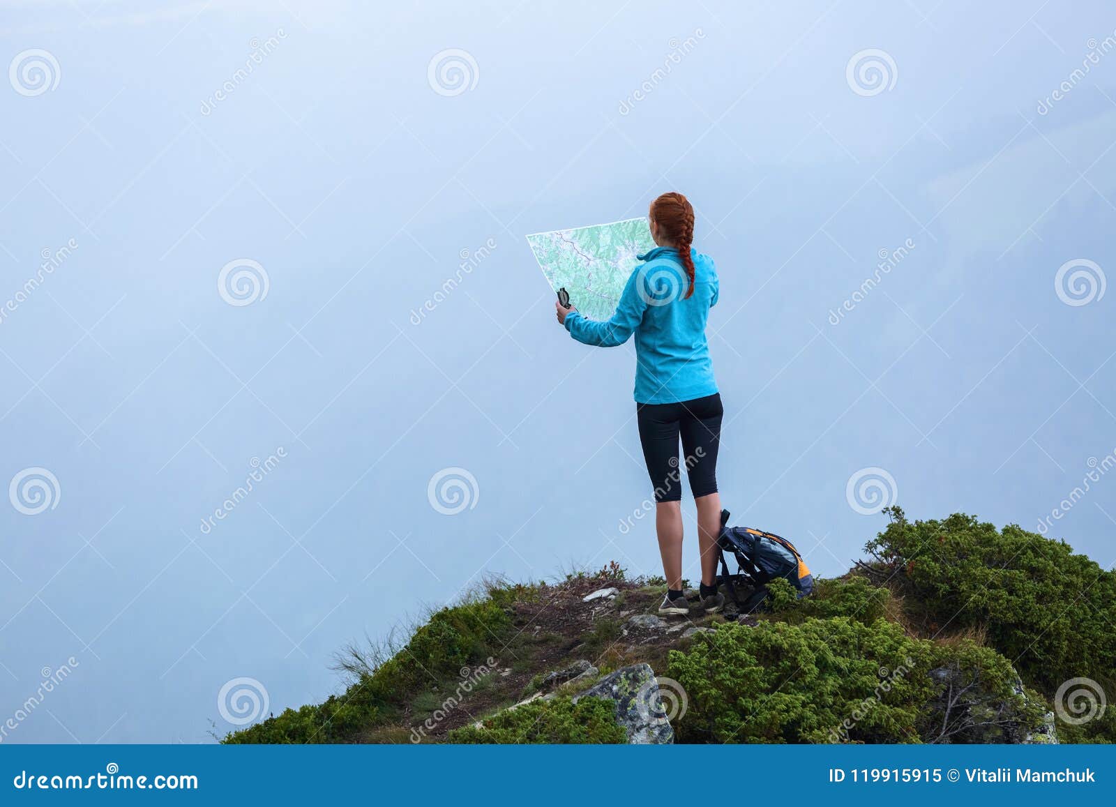 on the peak of the mountain the touris girl with the map and compass is searching for the way to dream. the horizon in the fog.