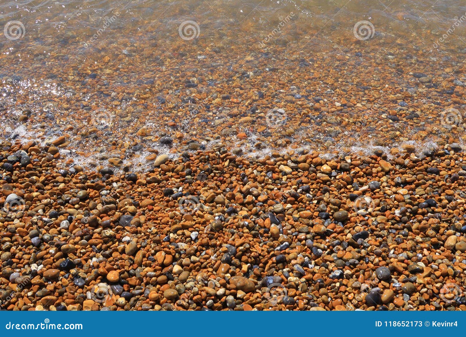 a pebbled beach with a small wave flowing over the sharp stones