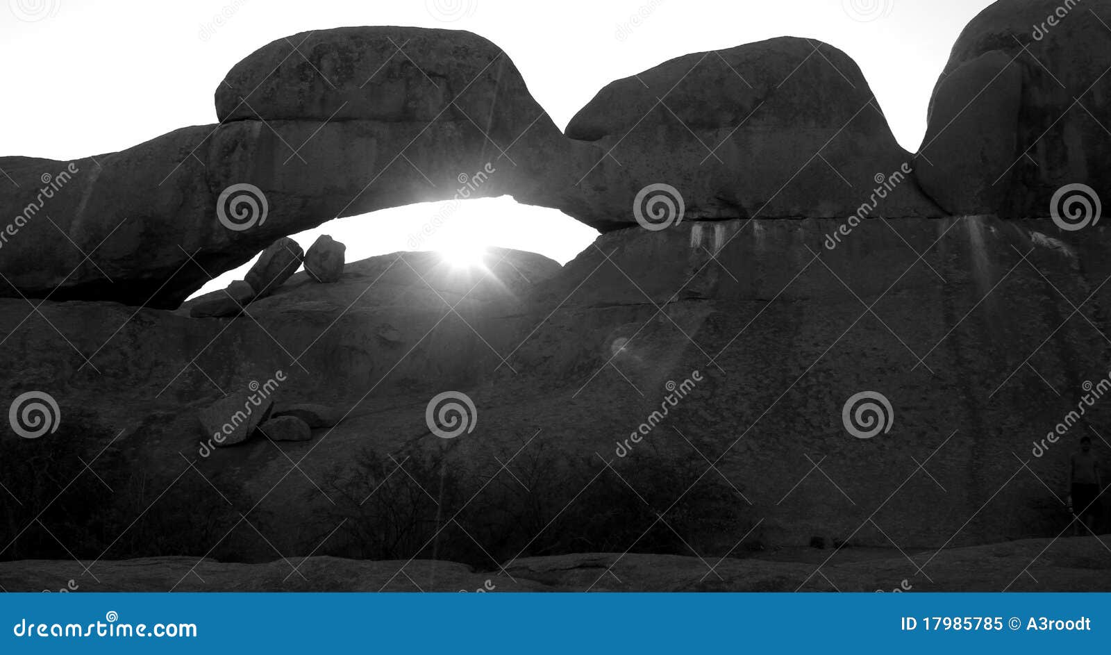 Peeping sun. Sun seen through bow in mountain rock at dusk in black and white.