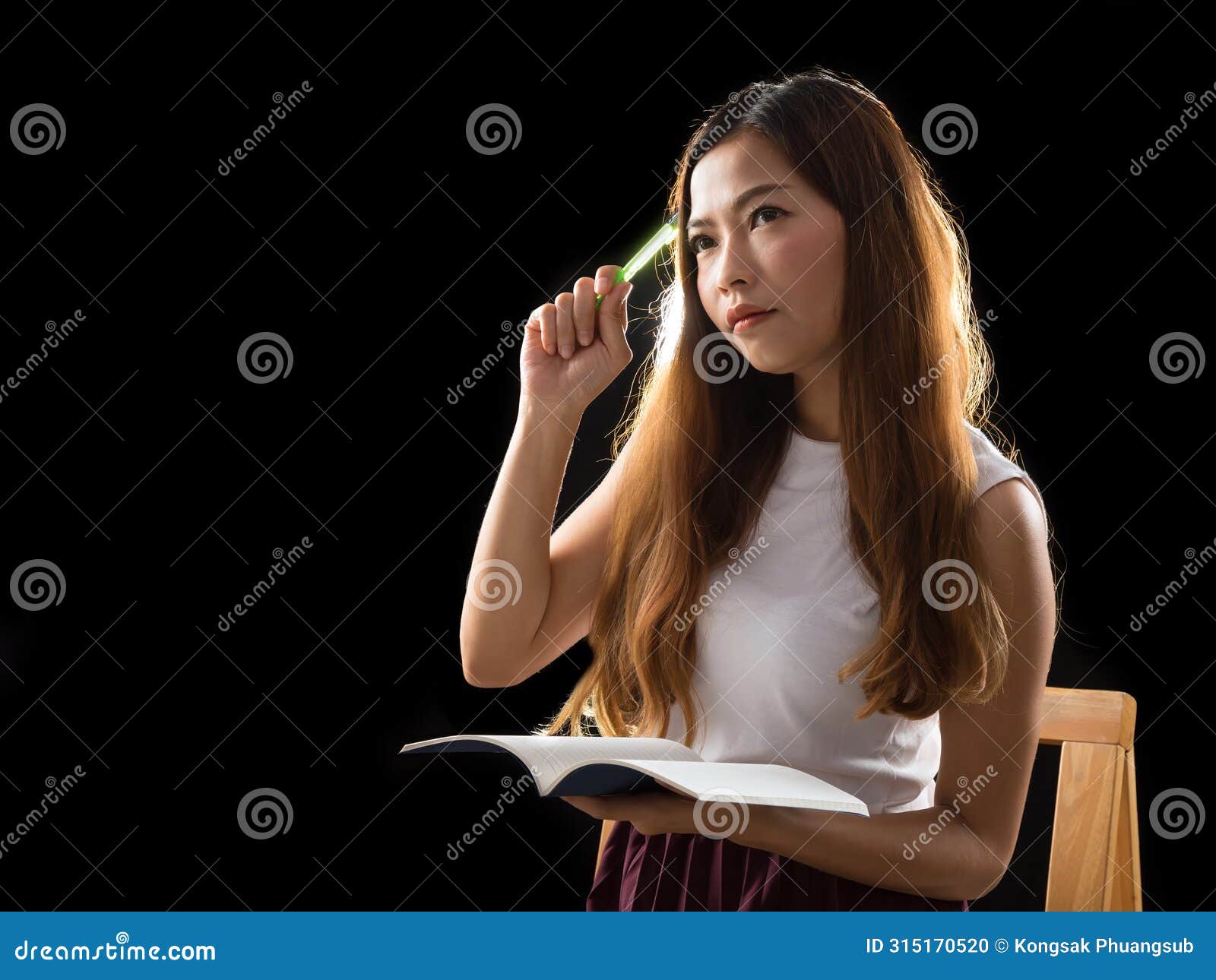 with a pen held pensively to her face, a young woman is deeply engrossed in a book, lost in thought and contemplation