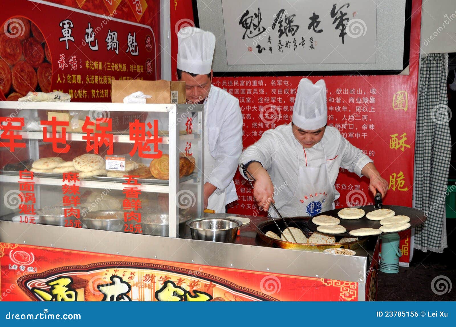 Pengzhou, China: Cozinheiros chefe que fazem o pão liso. Dois cozinheiros chefe vestidos nos uniformes e nos toques brancos em sua loja pequena em Pengzhou, China que prepara e que cozinha pães lisos chineses especiais usando um griddle e um wok