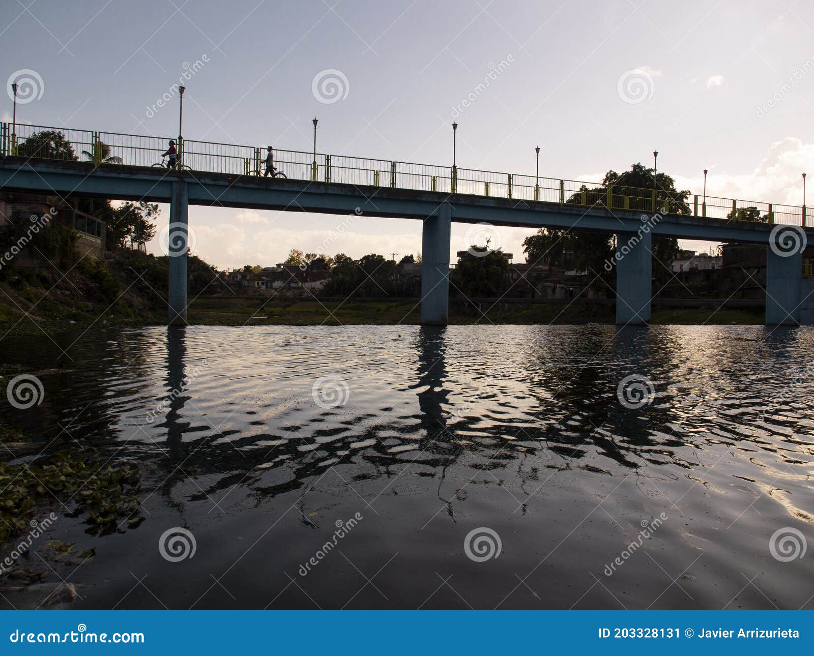 people crossing a river by a bridge, the bridge is reflected in the river