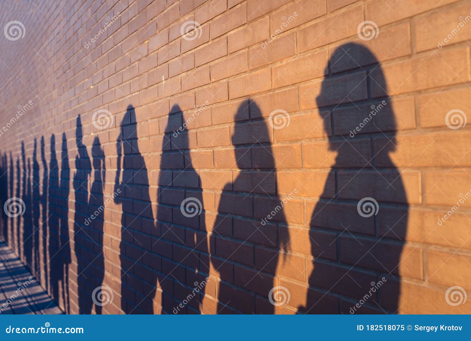 people crowd shadows lined up against a red brick wall. they are in a queue for changes in life. social distance, covid