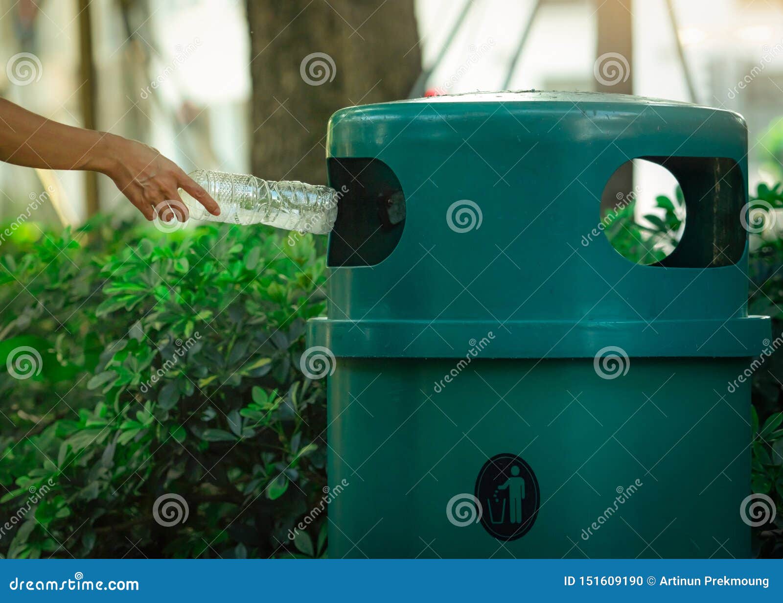 people hand throwing empty water bottle in recycle bin at park. green plastic recycle bin. man discard bottle in trash bin. waste
