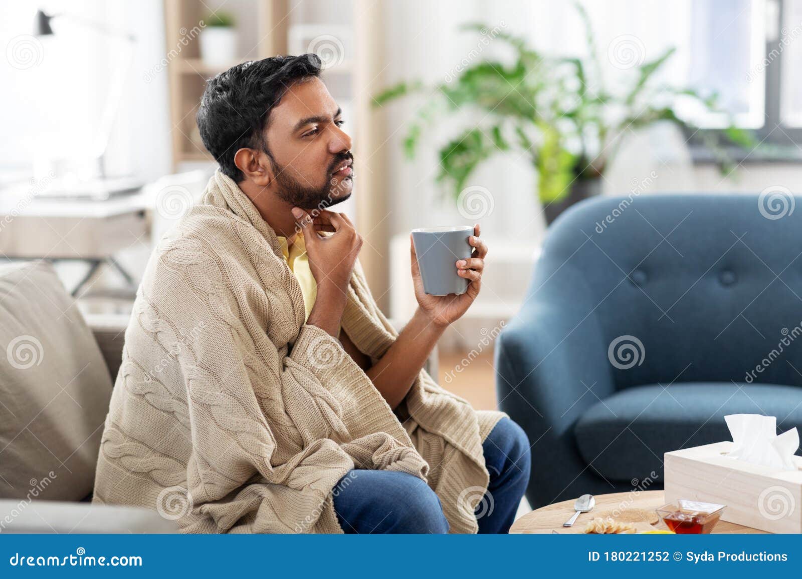 sick man with tea touching his sore throat at home