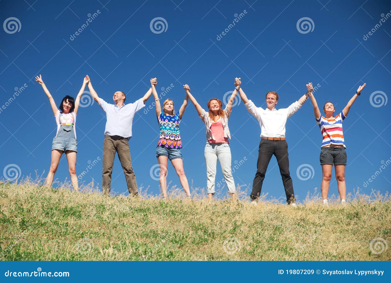 people on hill raise hands together